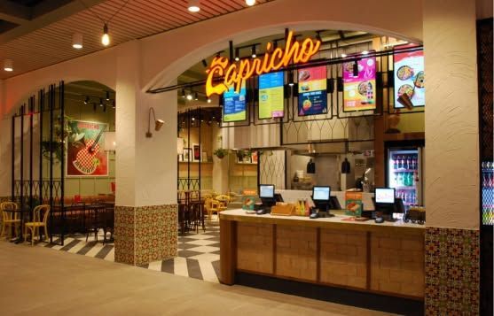 Restaurant counter with illuminated menu screens and warm tiled decor in a mall food court