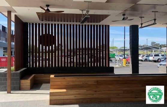 Outdoor covered seating area with wooden benches, vertical slats, and parking lot view beyond