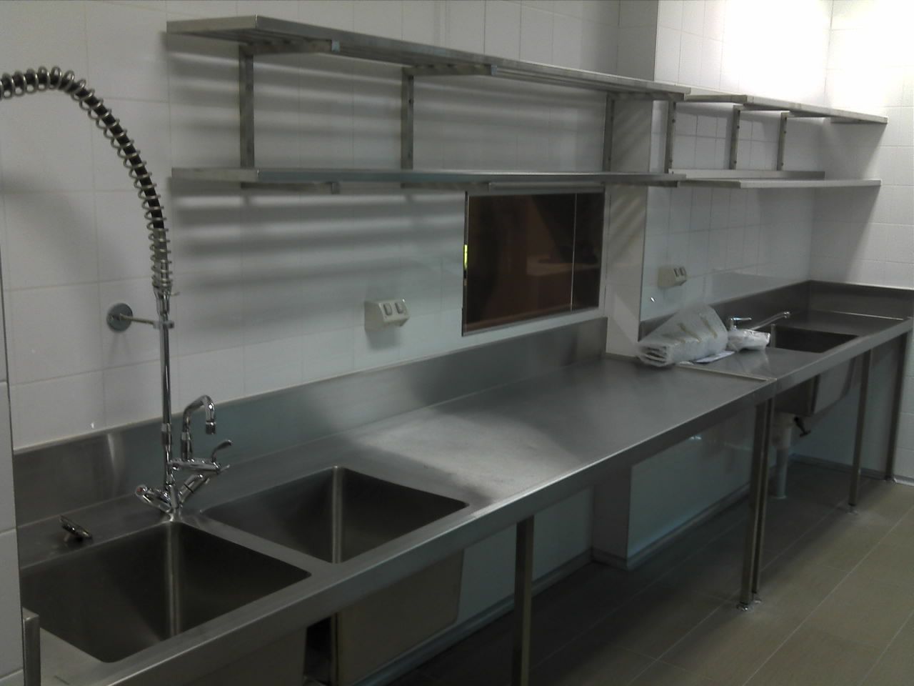 Stainless steel commercial kitchen sink area with faucet, counter, and wall shelves