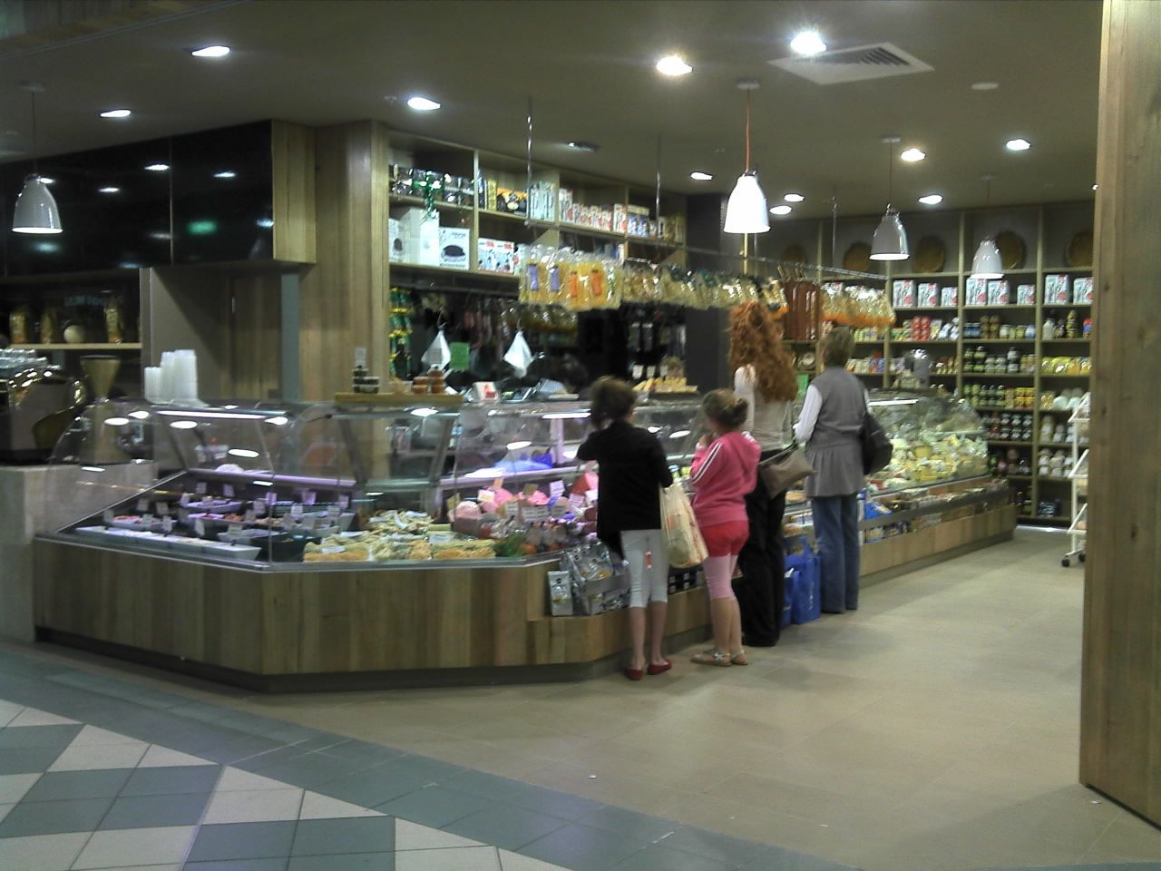 Delicatessen counter in a grocery store with shoppers browsing pastries and packaged goods