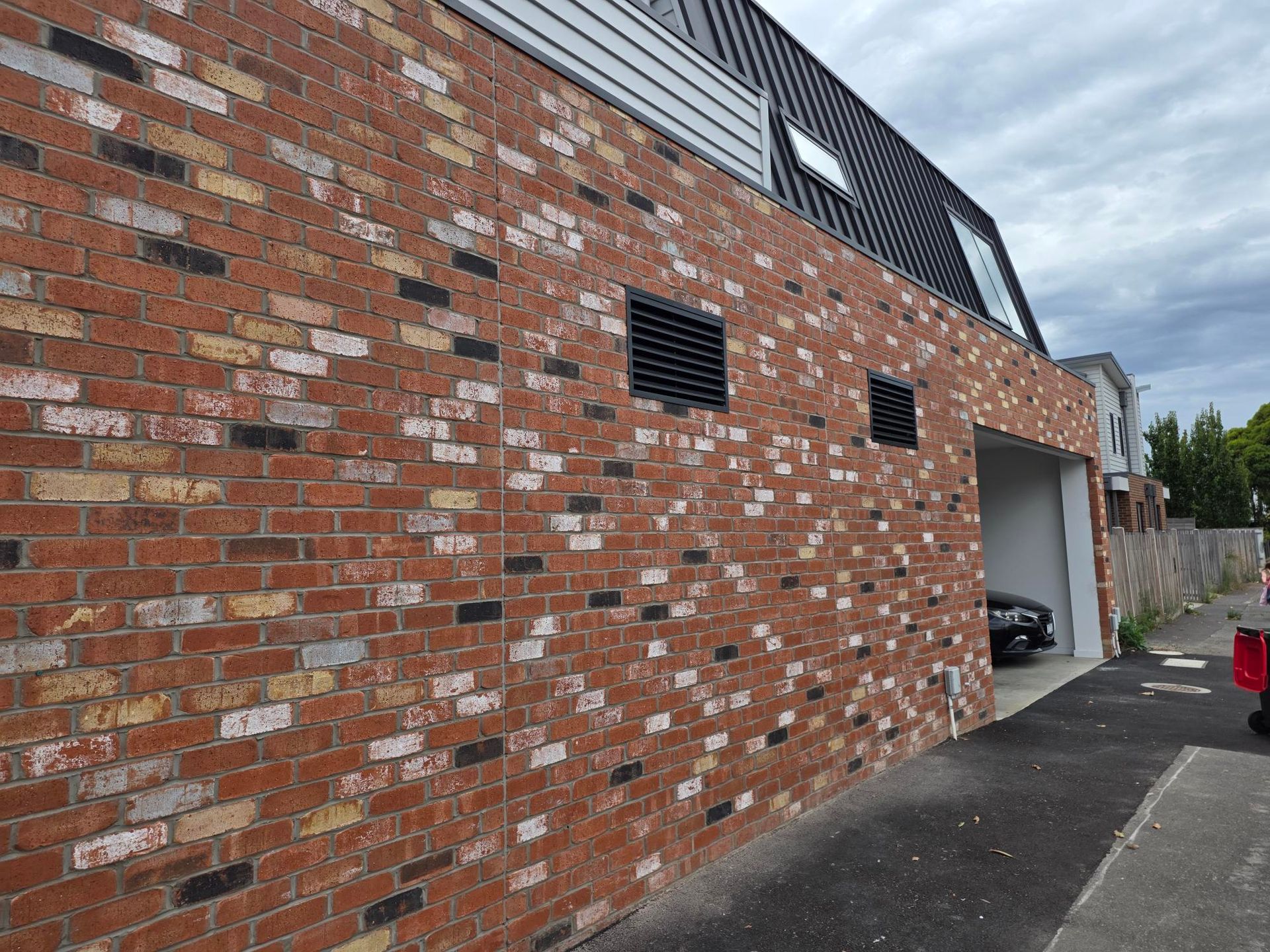 Brick building exterior with vents and open garage door beside a driveway