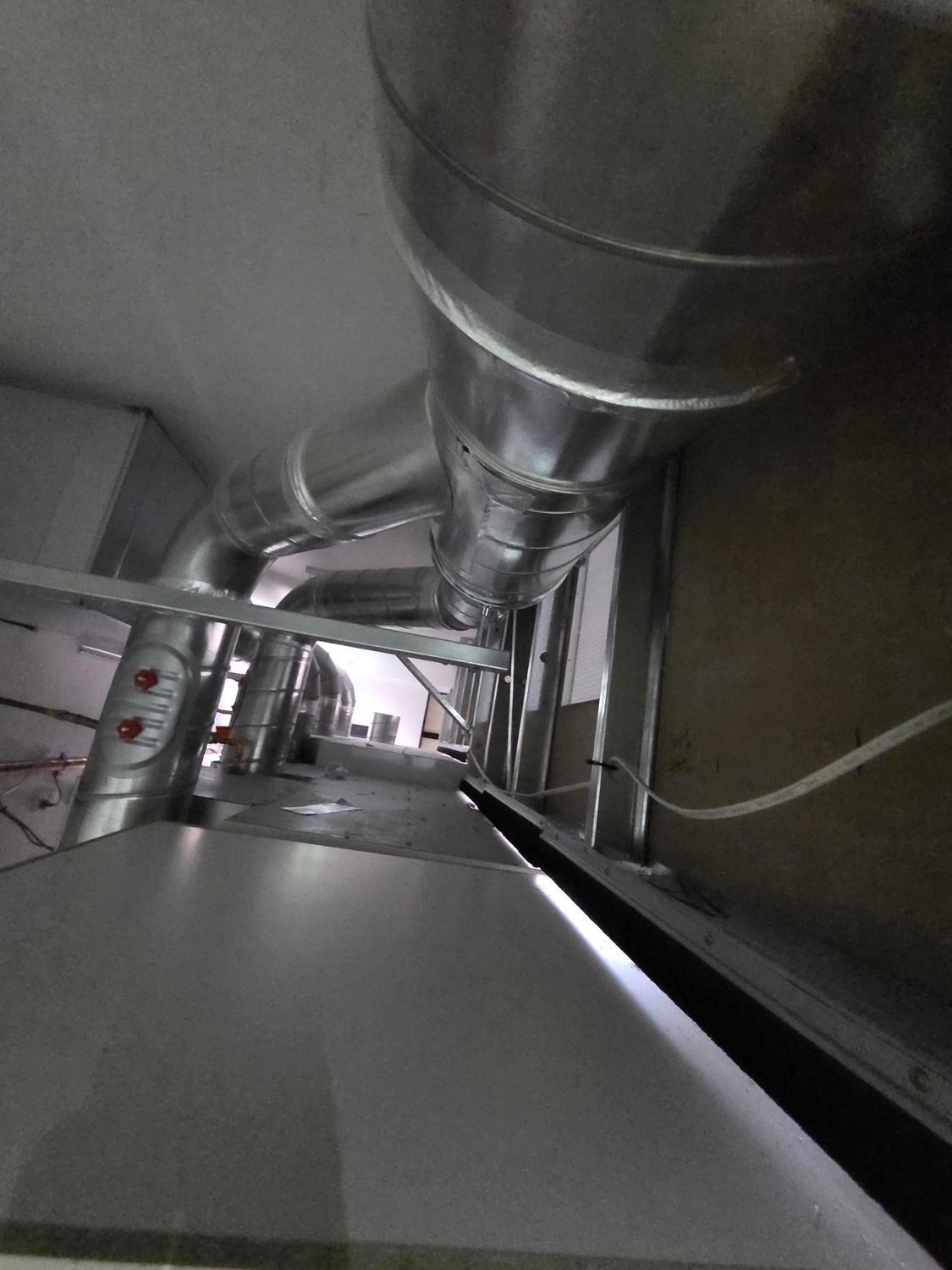 Tilted view down a metal ventilation duct with pipes and cables in an industrial interior