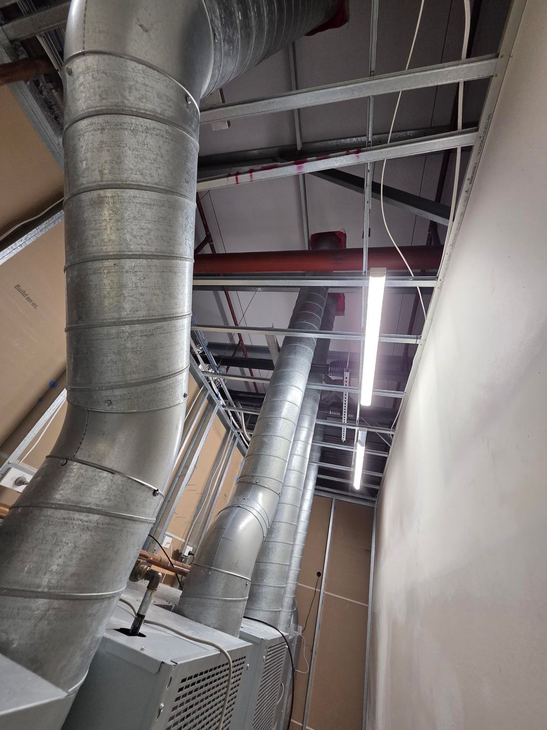 Industrial hallway with exposed silver ductwork and ceiling pipes above a narrow corridor.