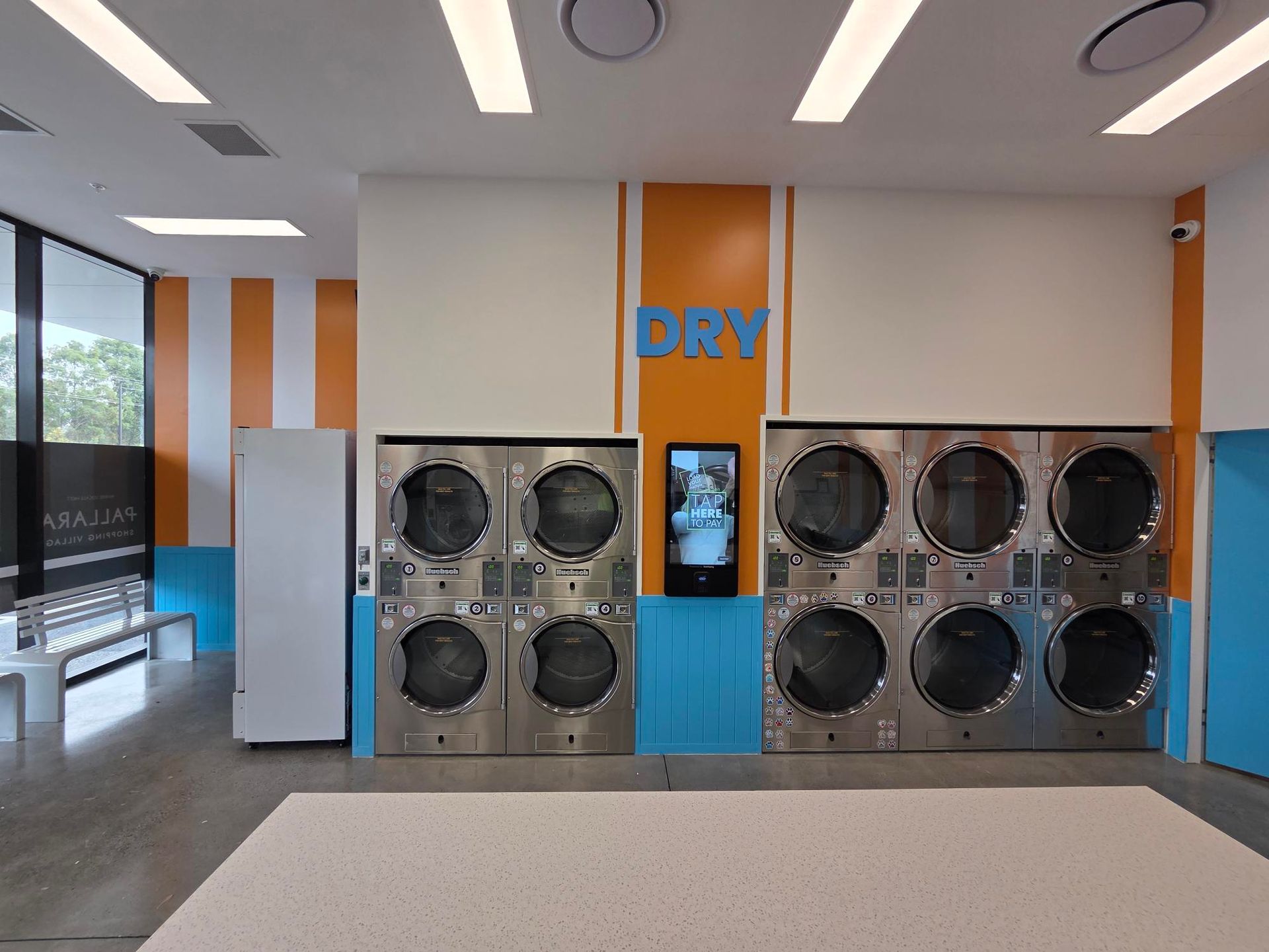 Laundry room with rows of stainless steel dryers and washers, white walls, and orange accents