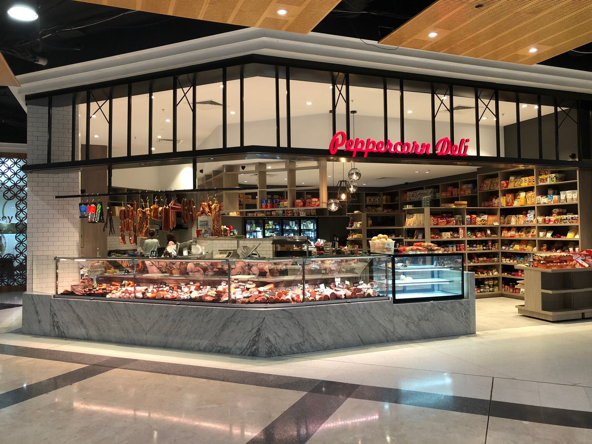Modern bakery and deli counter with glass display cases and red signage in a mall setting