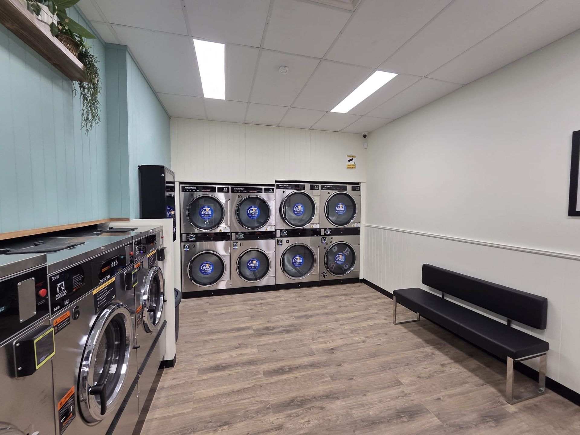 Laundry room with stacked washers and dryers, black bench, and white walls under fluorescent lights