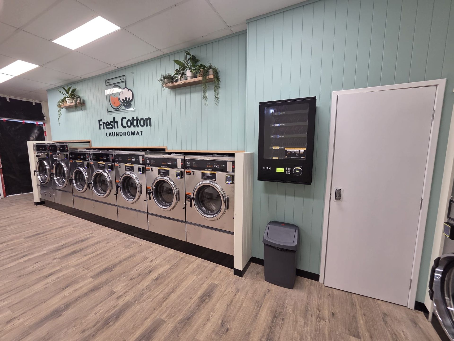 Laundry room with row of front-load washers, pale blue wall, and white door