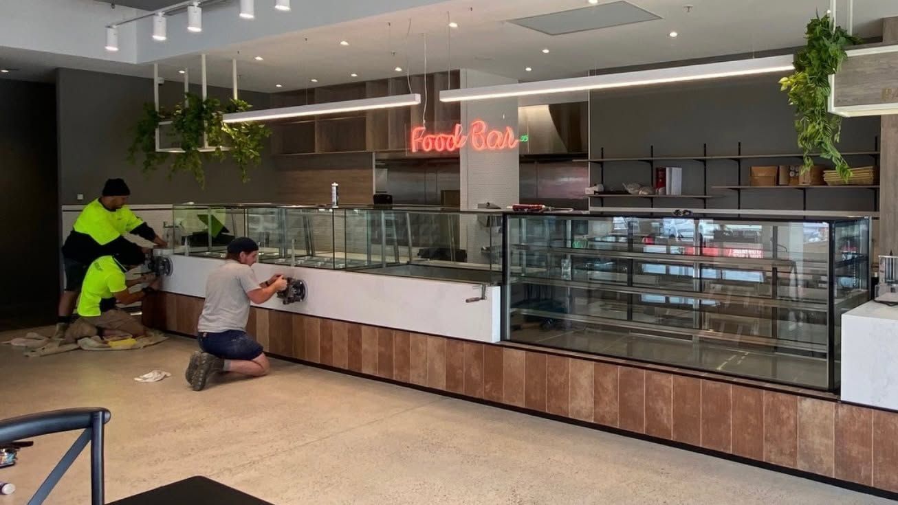 Modern food court counter with glass display cases and two workers near the register