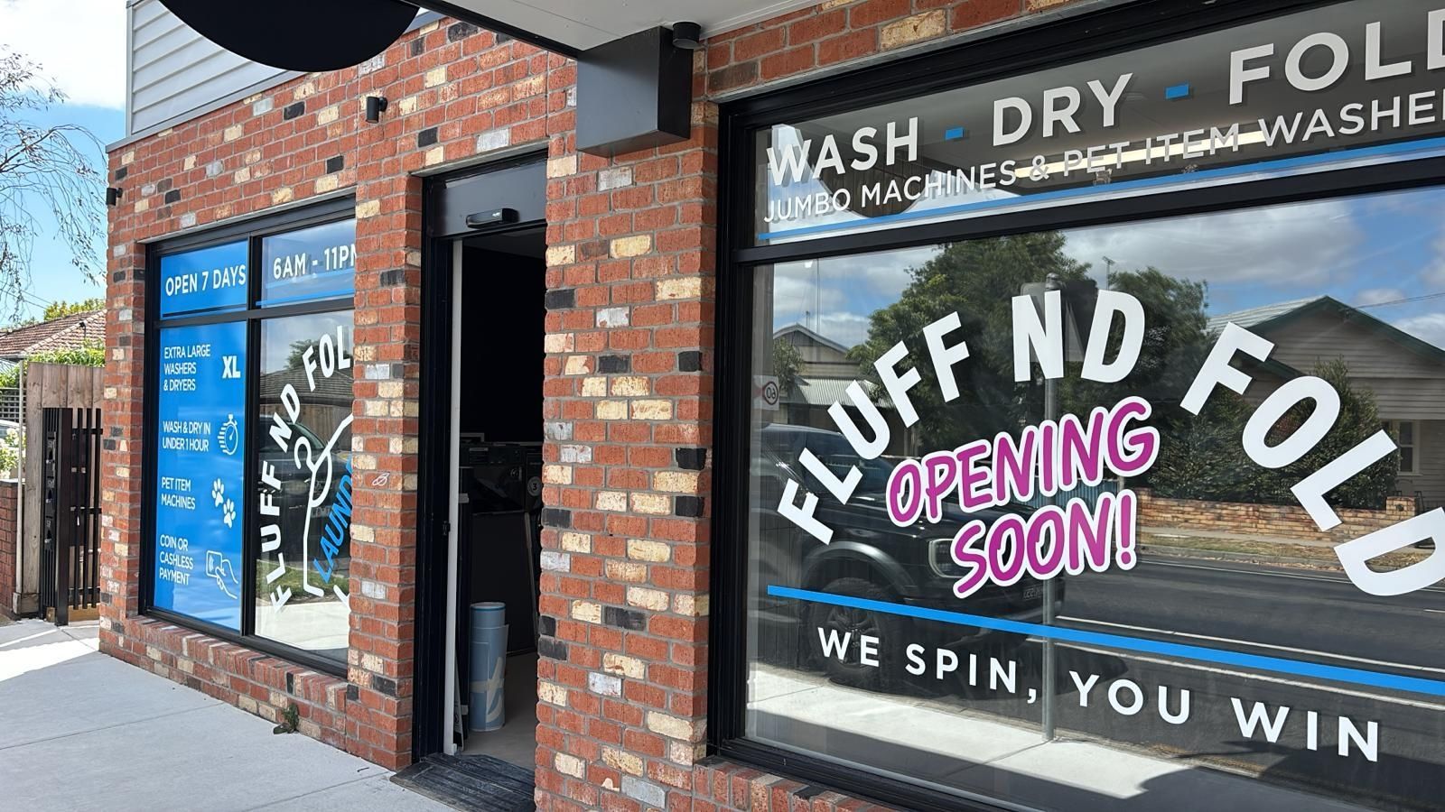 Storefront with brick exterior and window signs reading “Fluff N Fold” and “Opening Soon.”