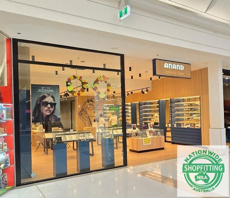 Anand eyewear store entrance in a mall, with glass displays and a shopper in sunglasses.