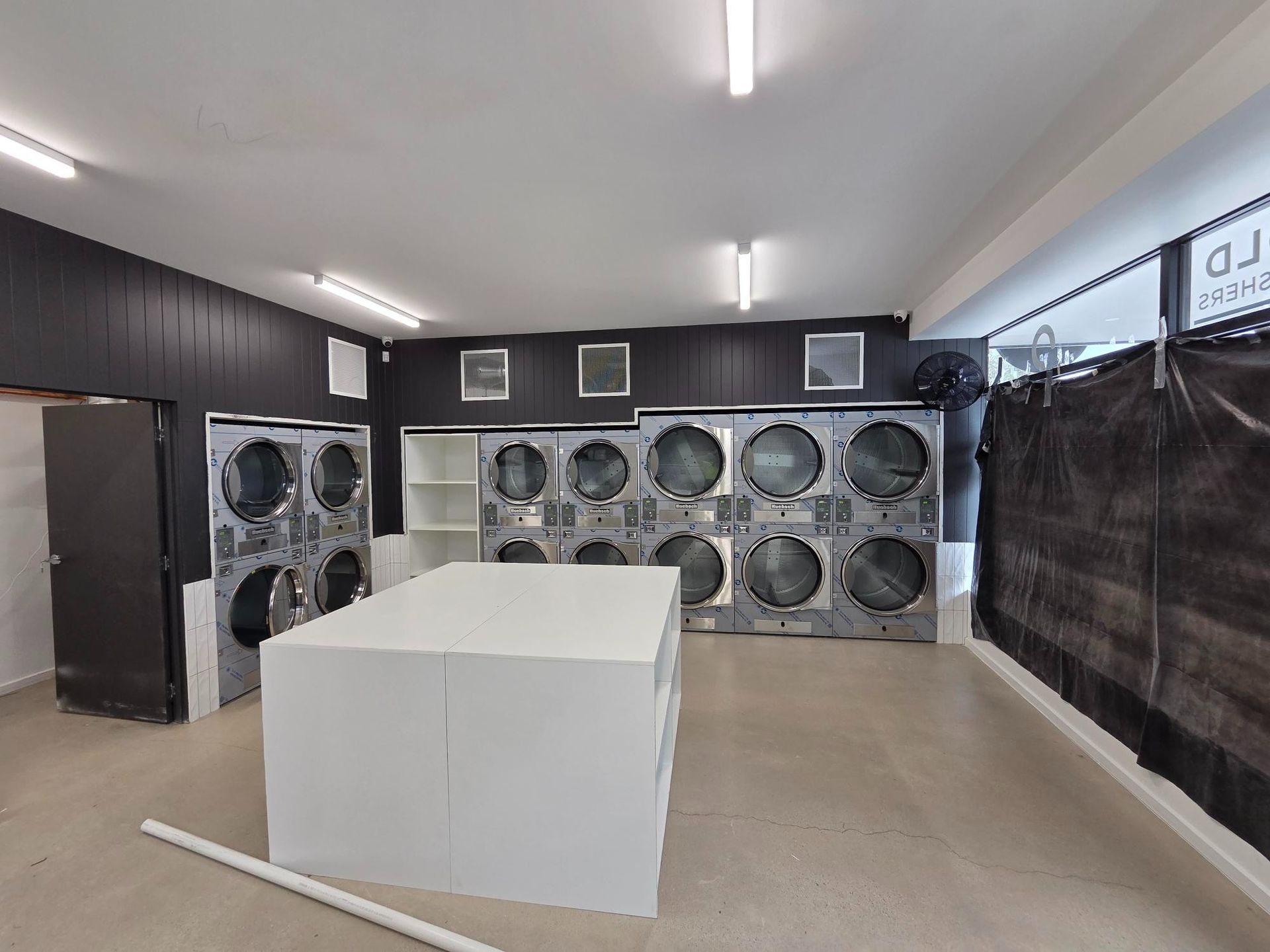 Indoor workshop with large industrial fans, black walls, bright ceiling lights, and a white box in the foreground