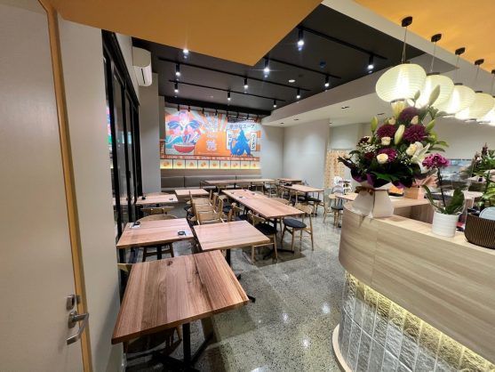 Empty café dining area with wooden tables, black chairs, and a floral counter under warm pendant lights.