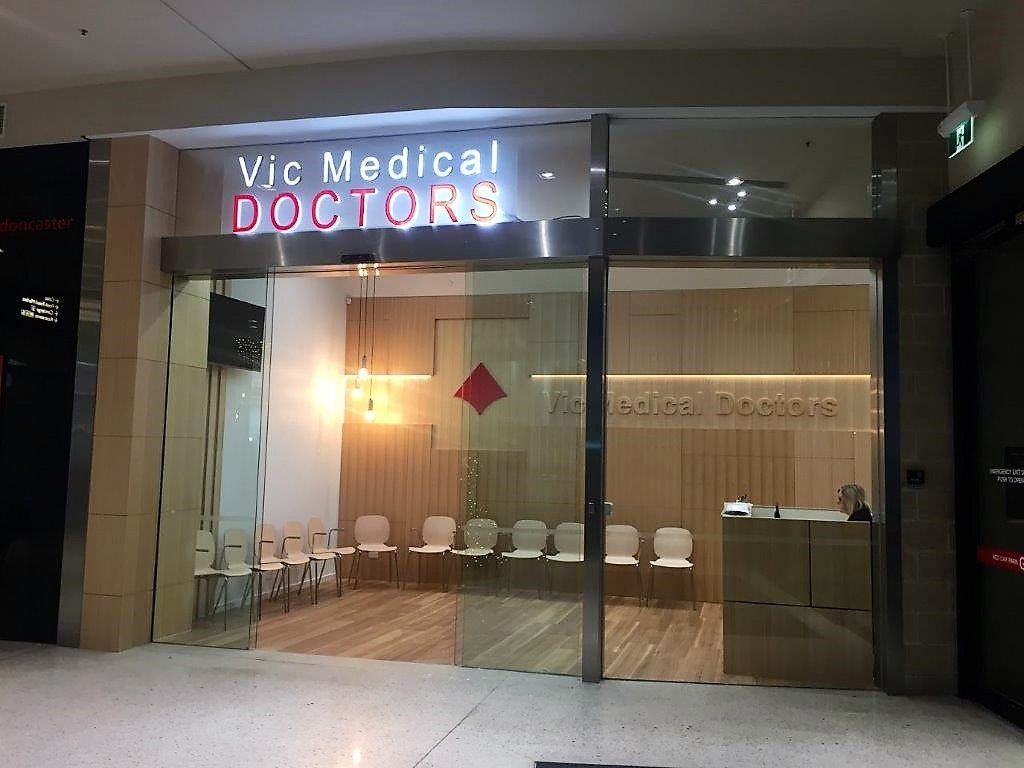 Glass-front medical office lobby with “Vic Medical DOCTORS” sign and waiting chairs inside