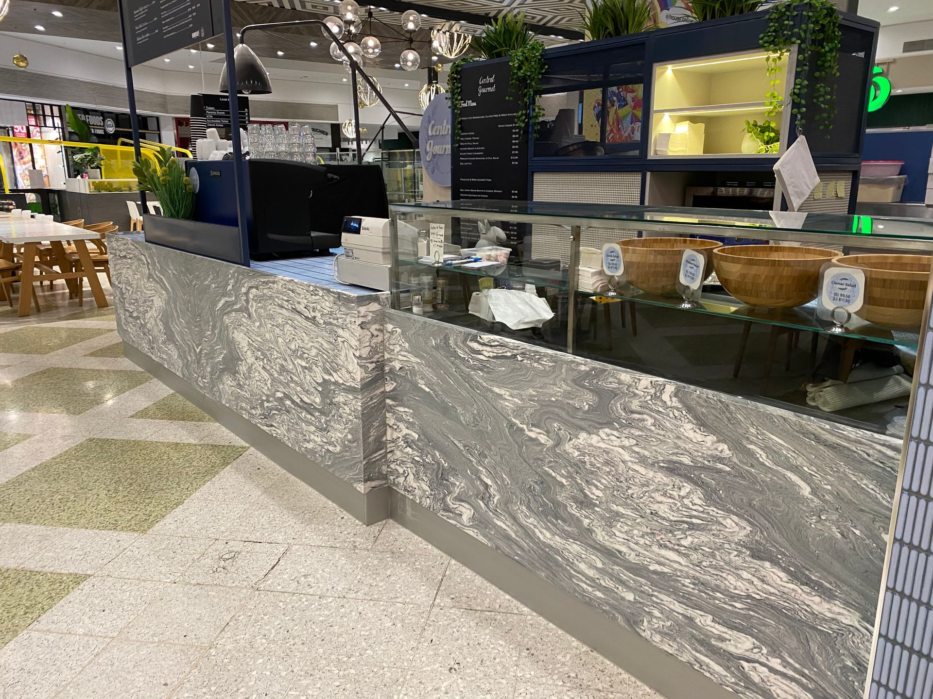 Modern café counter with gray marble panels, glass display cases, and warm overhead lighting