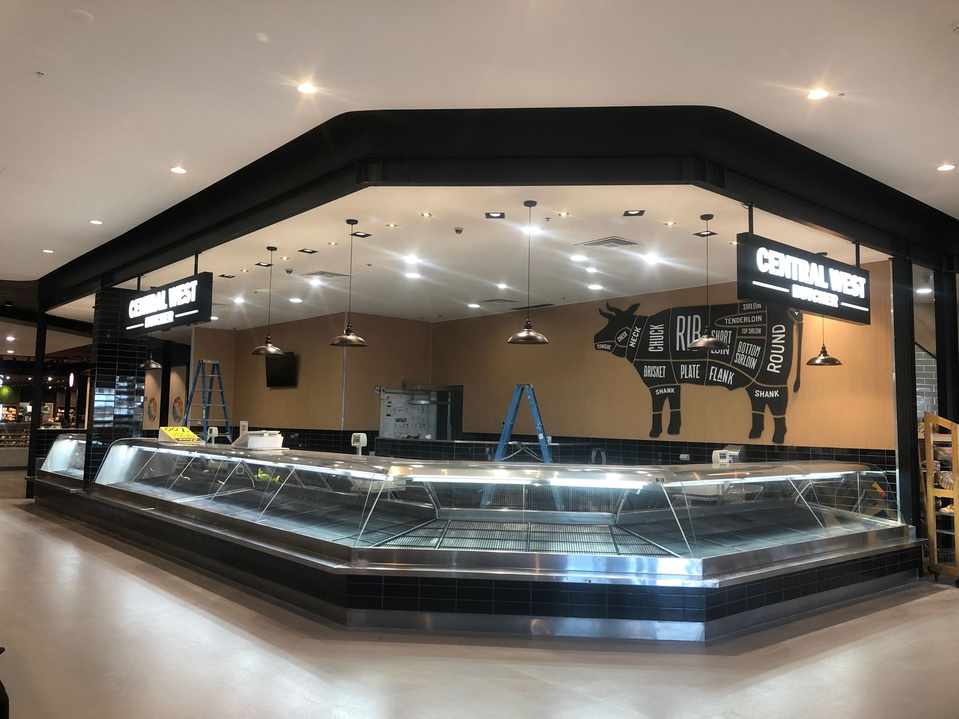 Empty deli counter inside a modern market with bright ceiling lights and dark wood trim