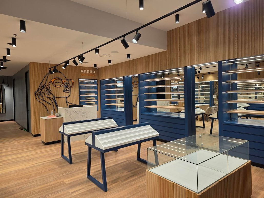 Empty retail clothing store with blue shelving, wood floors, and display tables under track lighting Empty modern retail store interior with wooden floors, blue wall shelving, and display tables.