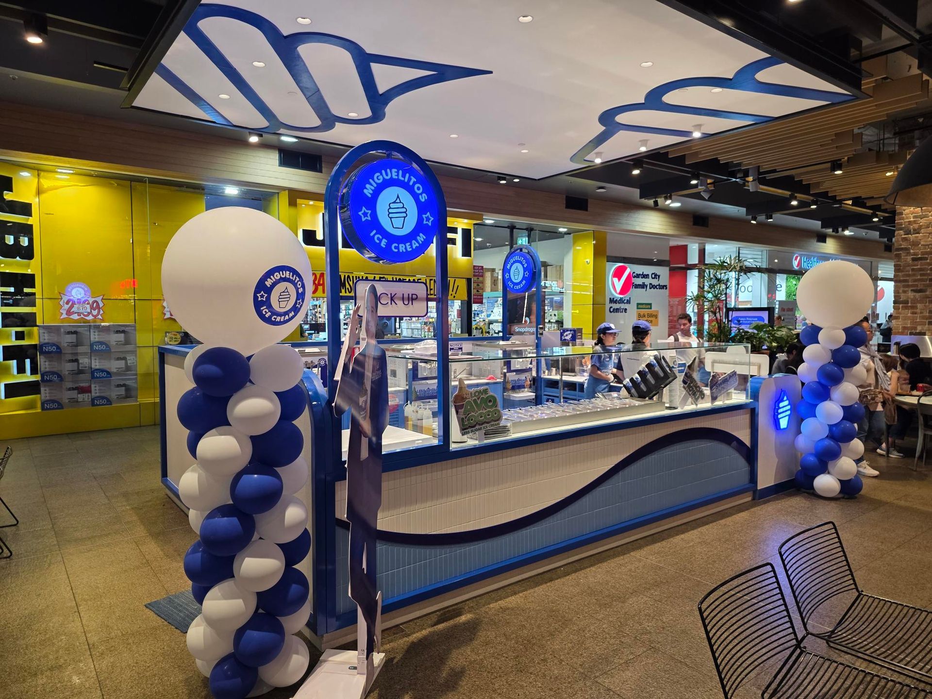 Blue-and-white balloon-decorated storefront kiosk in a mall corridor with displays inside