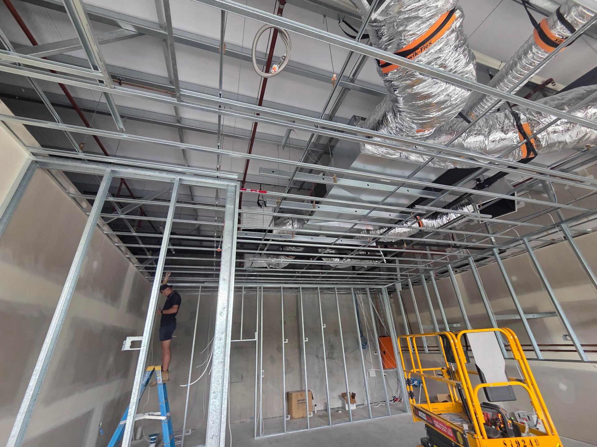 Industrial room with exposed HVAC ductwork, metal piping, and a ladder near stacked boxes