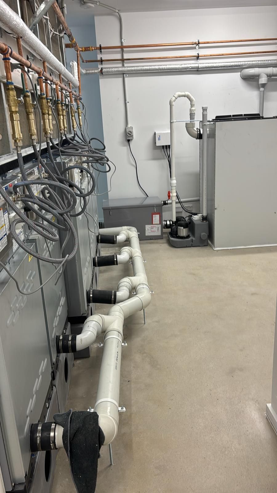 Industrial room with pipes, cables, and equipment along a concrete floor.