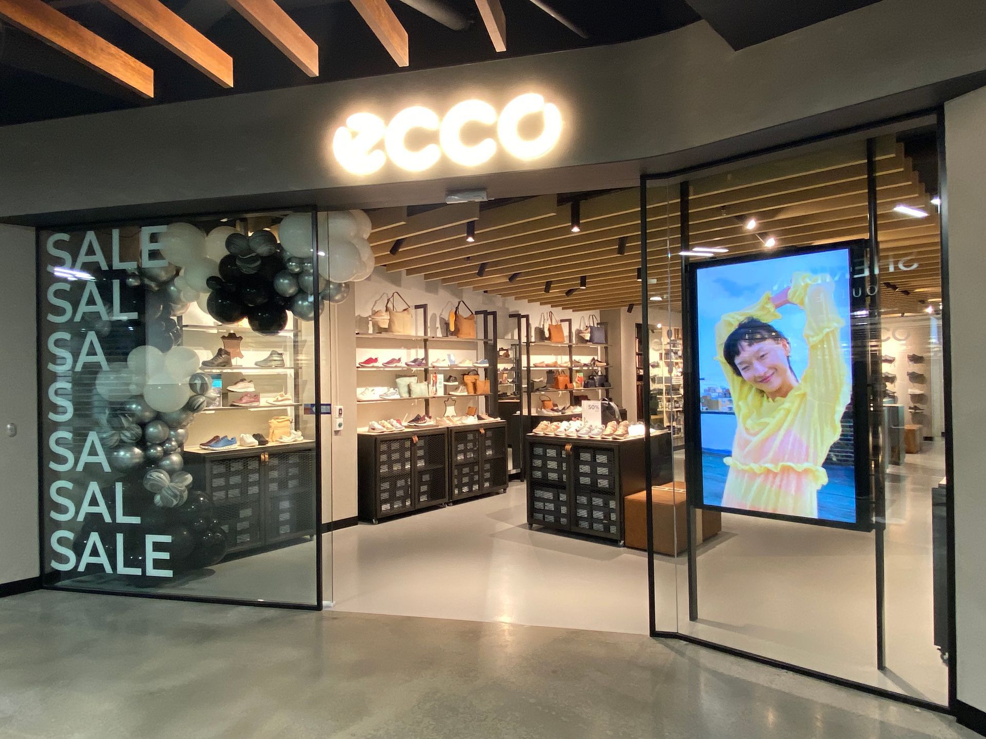 ECCO shoe store entrance with SALE signs, open doors, and a colorful display screen