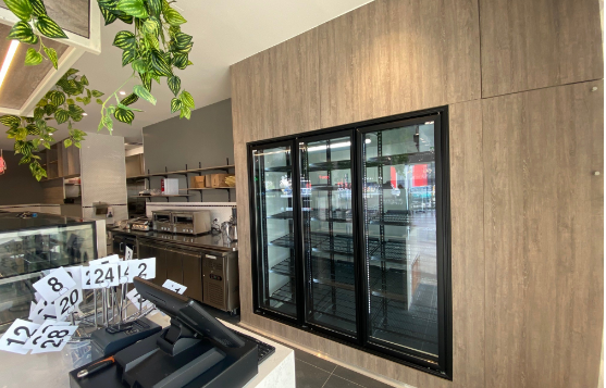 Modern café interior with wood wall, black-framed display fridge, and hanging greenery