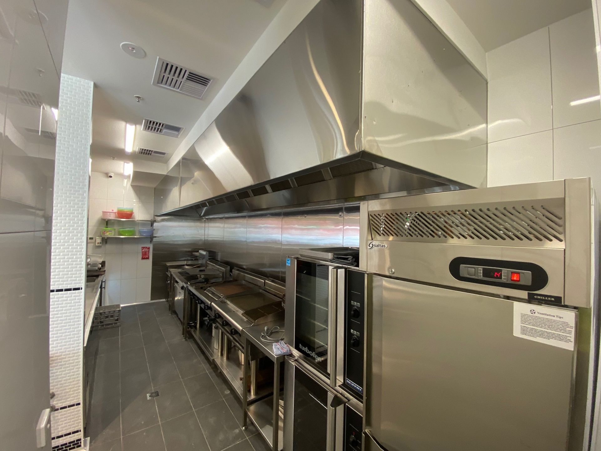 Stainless steel commercial kitchen with long cooking line and exhaust hood in a narrow corridor