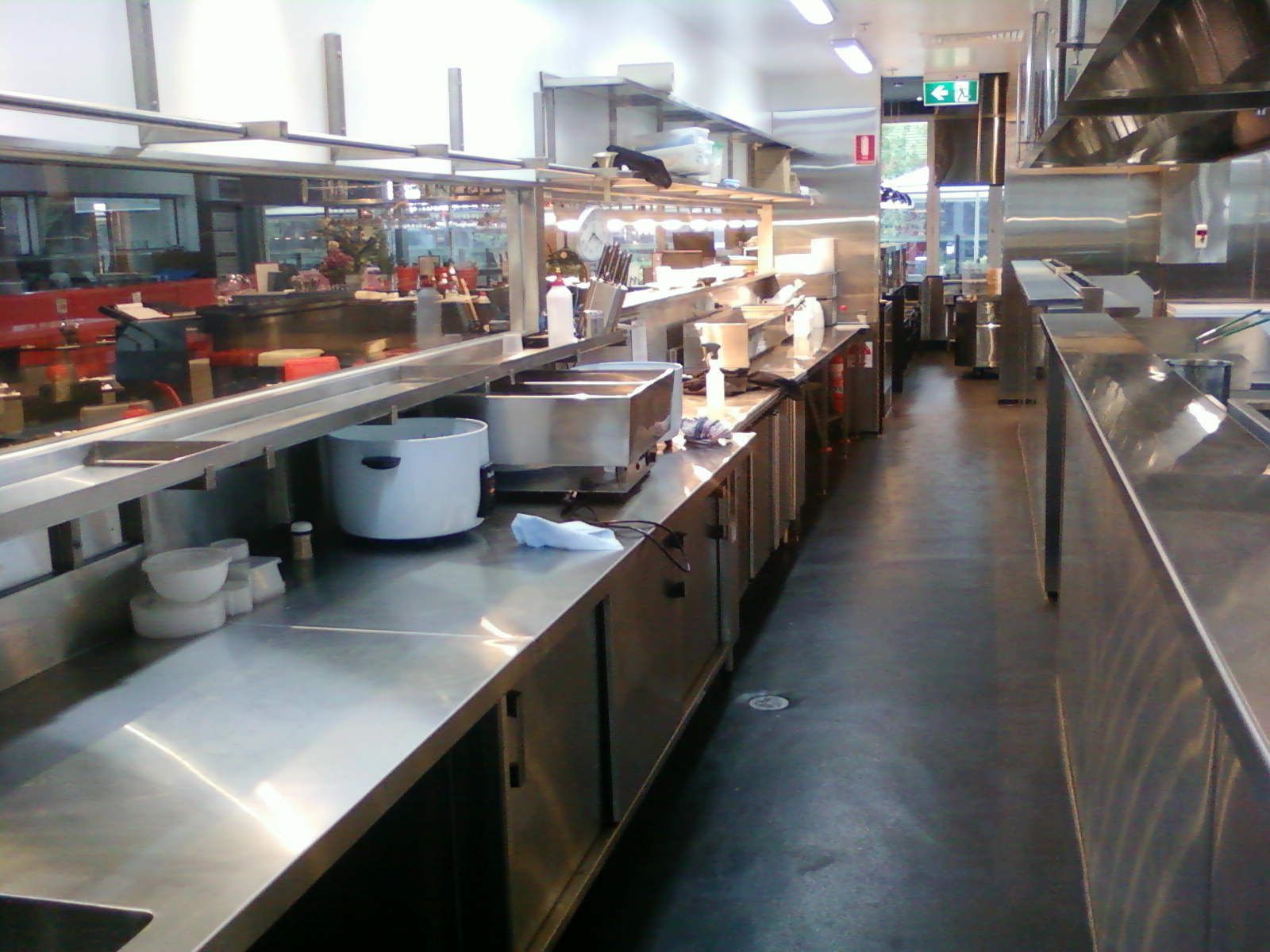 Stainless steel restaurant kitchen with counters, pots, and a serving line under bright lights.