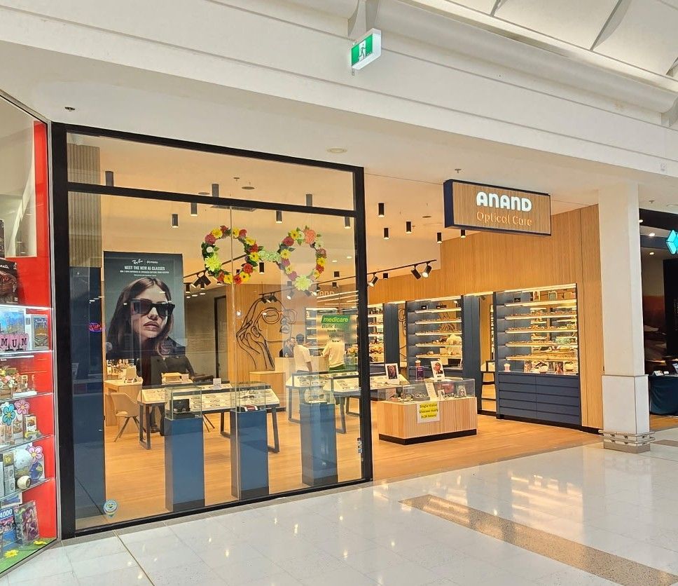 Modern eyewear store storefront with glass entrance, lit displays, and a woman’s face on a poster inside