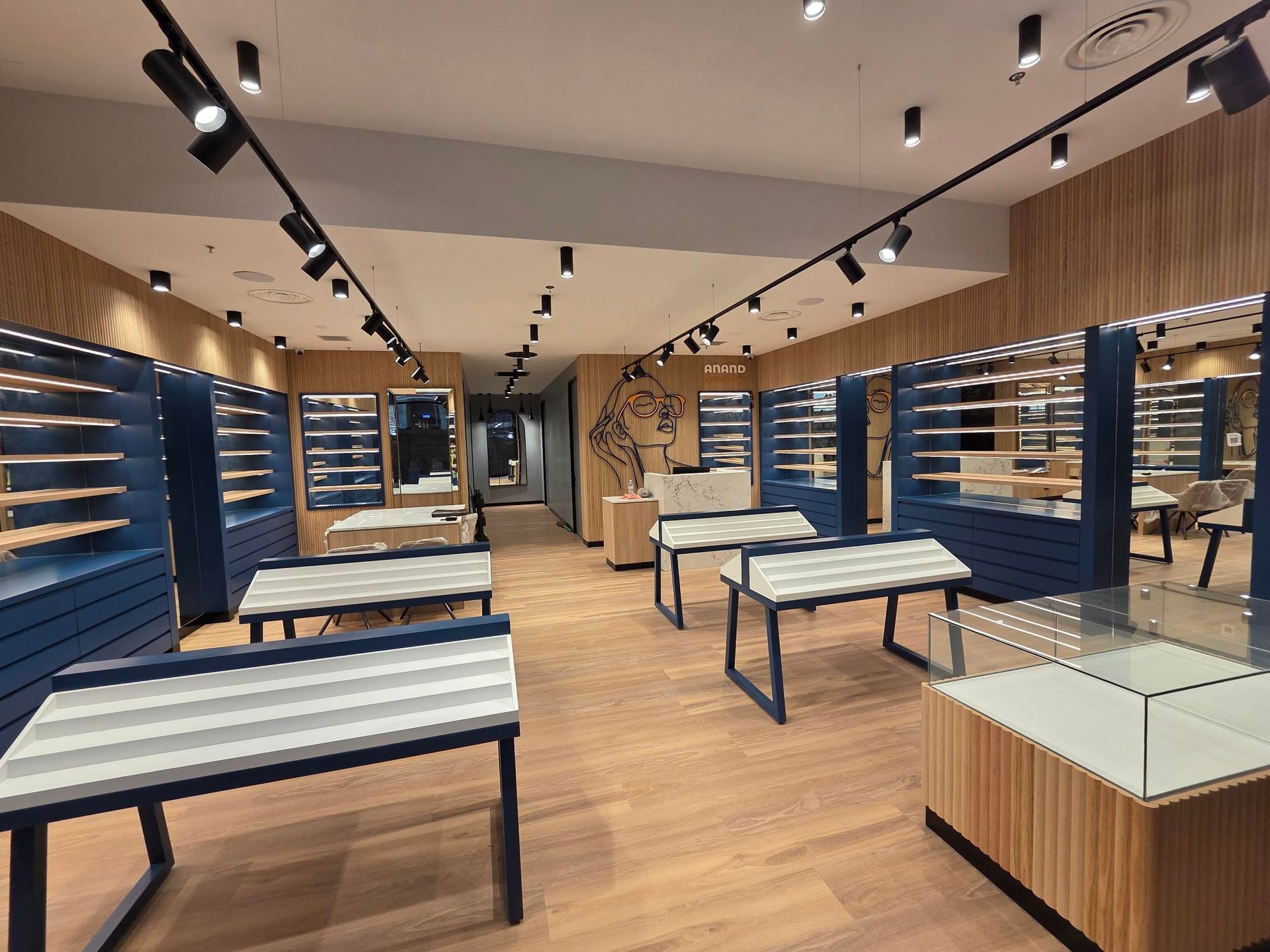 Empty modern retail store with wooden floors, blue wall shelves, and display tables under track lighting
