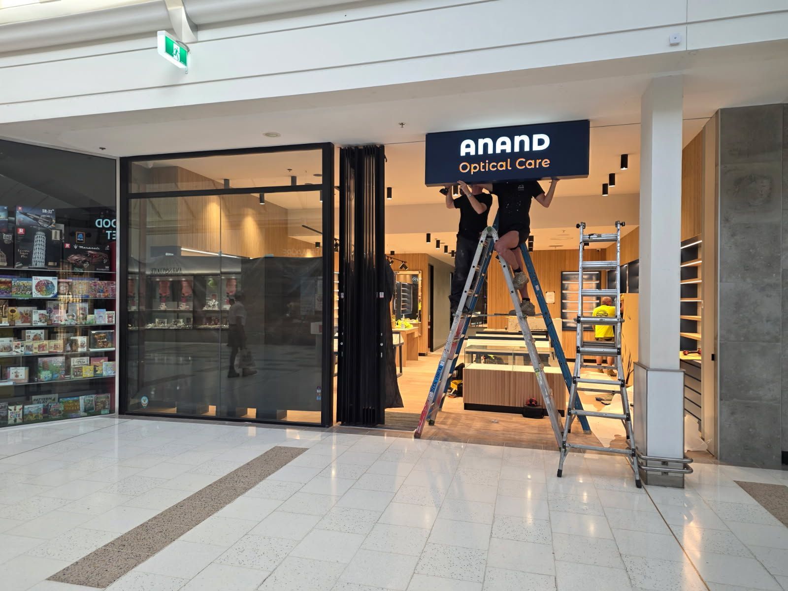 Entrance to Anand Optical Care storefront with ladders and shop interior visible
