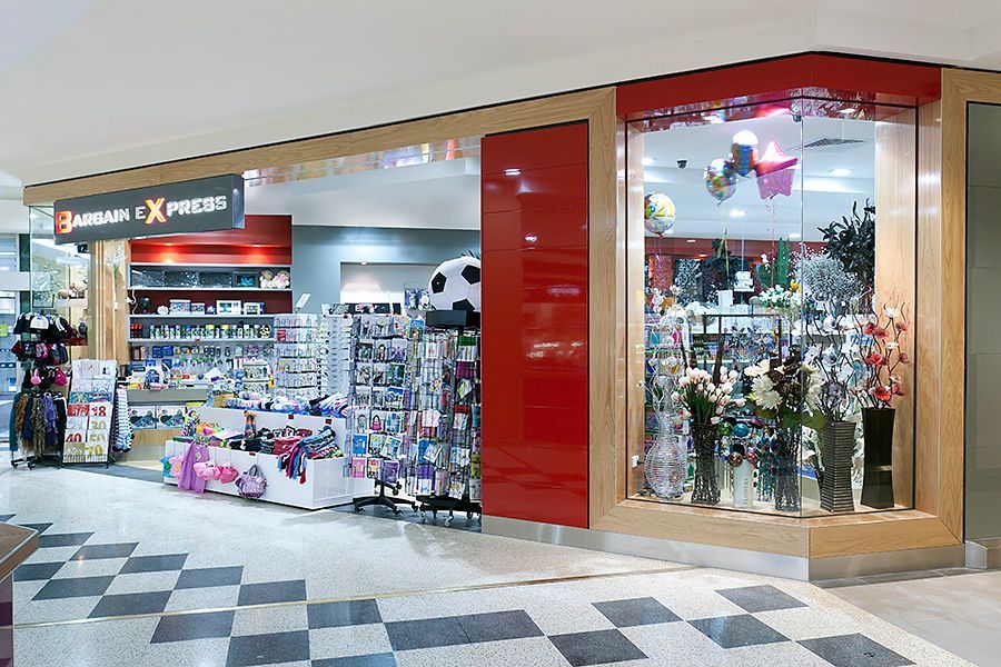 Shopping mall kiosk selling gifts and toys, with red trim and colorful displays behind glass.
