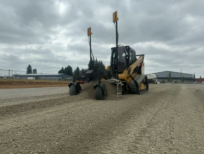 Yellow excavator on a gravel surface near a pile of gravel and trees.