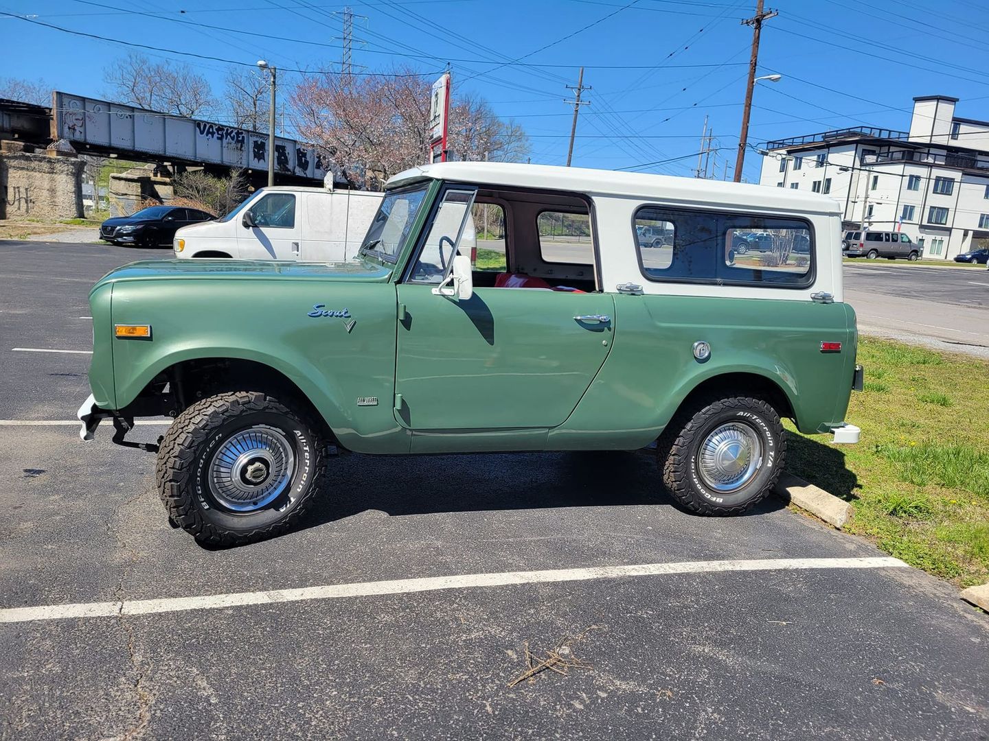 A vintage green International Harvester Scout with a white roof parked in an outdoor lot on a sunny day.