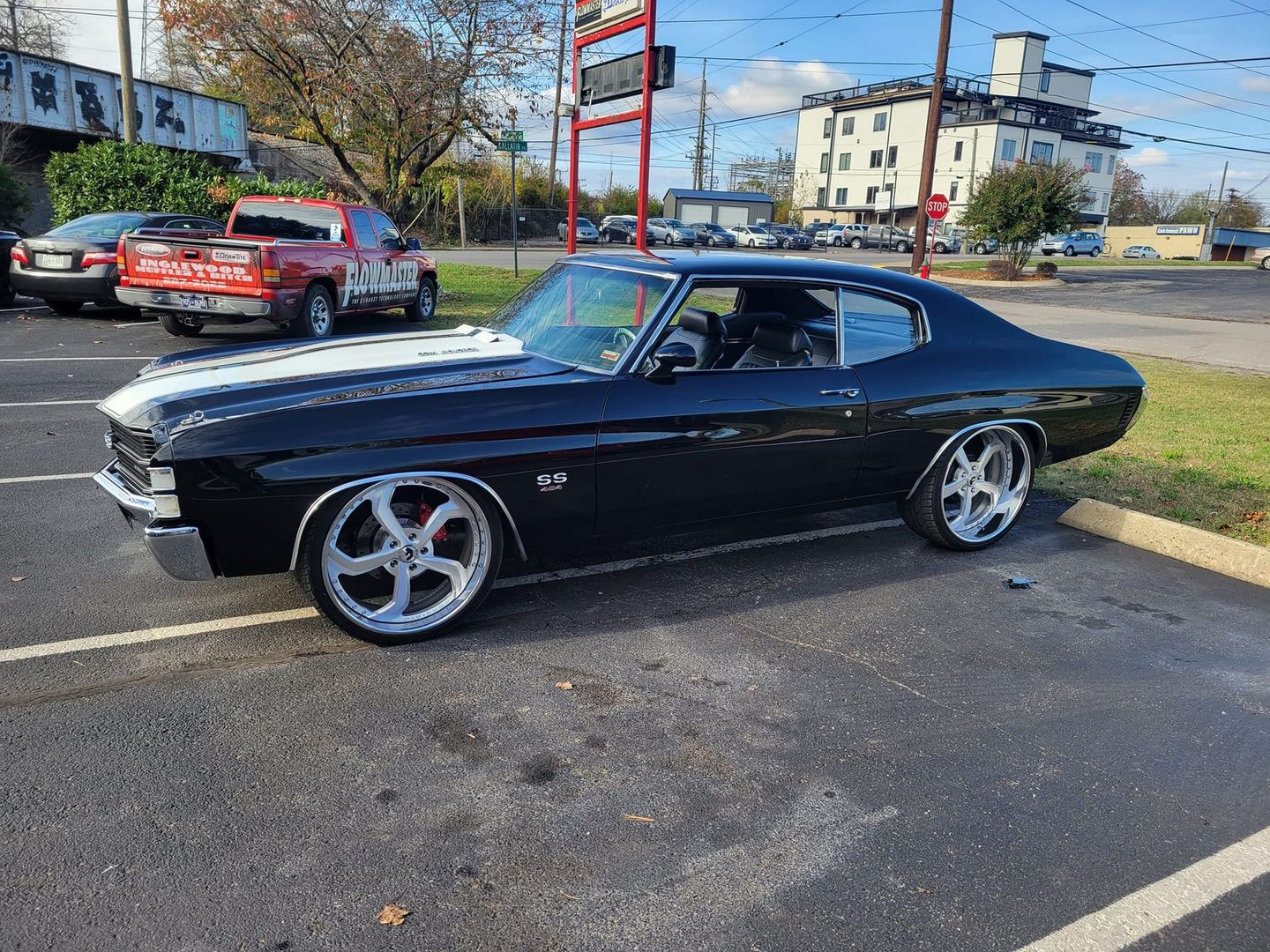 A black Chevrolet Chevelle SS with white racing stripes and large chrome wheels parked in an outdoor parking lot.