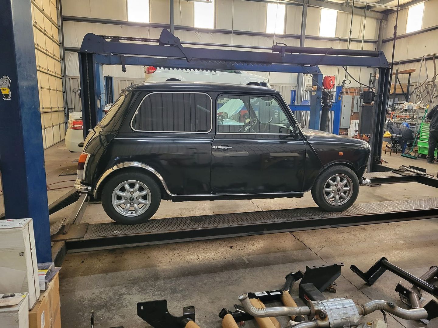 A black classic Mini Cooper parked on a metal lift inside an auto repair shop.