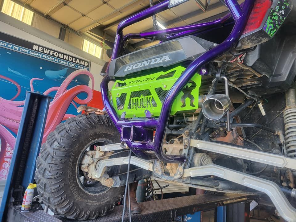 The rear of a Honda ATV with a purple frame and a bright green, custom “Hulk” branded radiator guard on a vehicle lift.