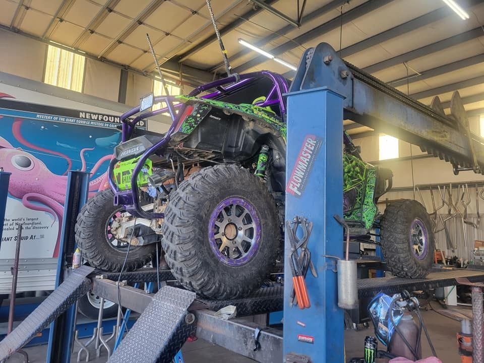 A green and purple off-road vehicle sits raised on a blue automotive lift inside a repair shop.