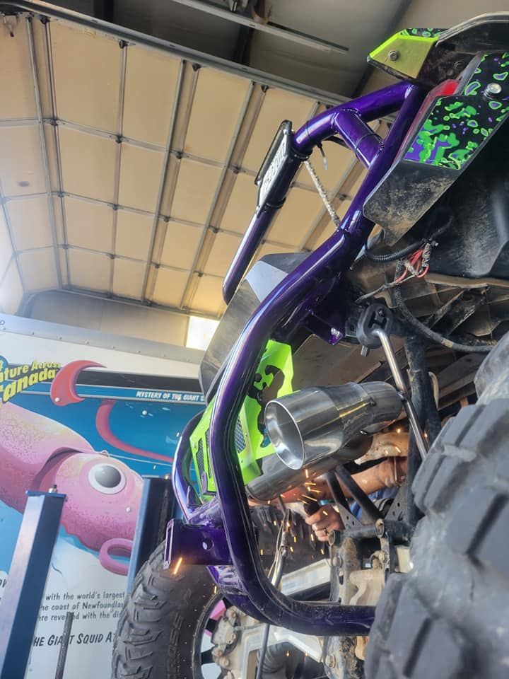 Low-angle shot of a purple-framed off-road vehicle with a silver exhaust, parked near a colorful wall mural.
