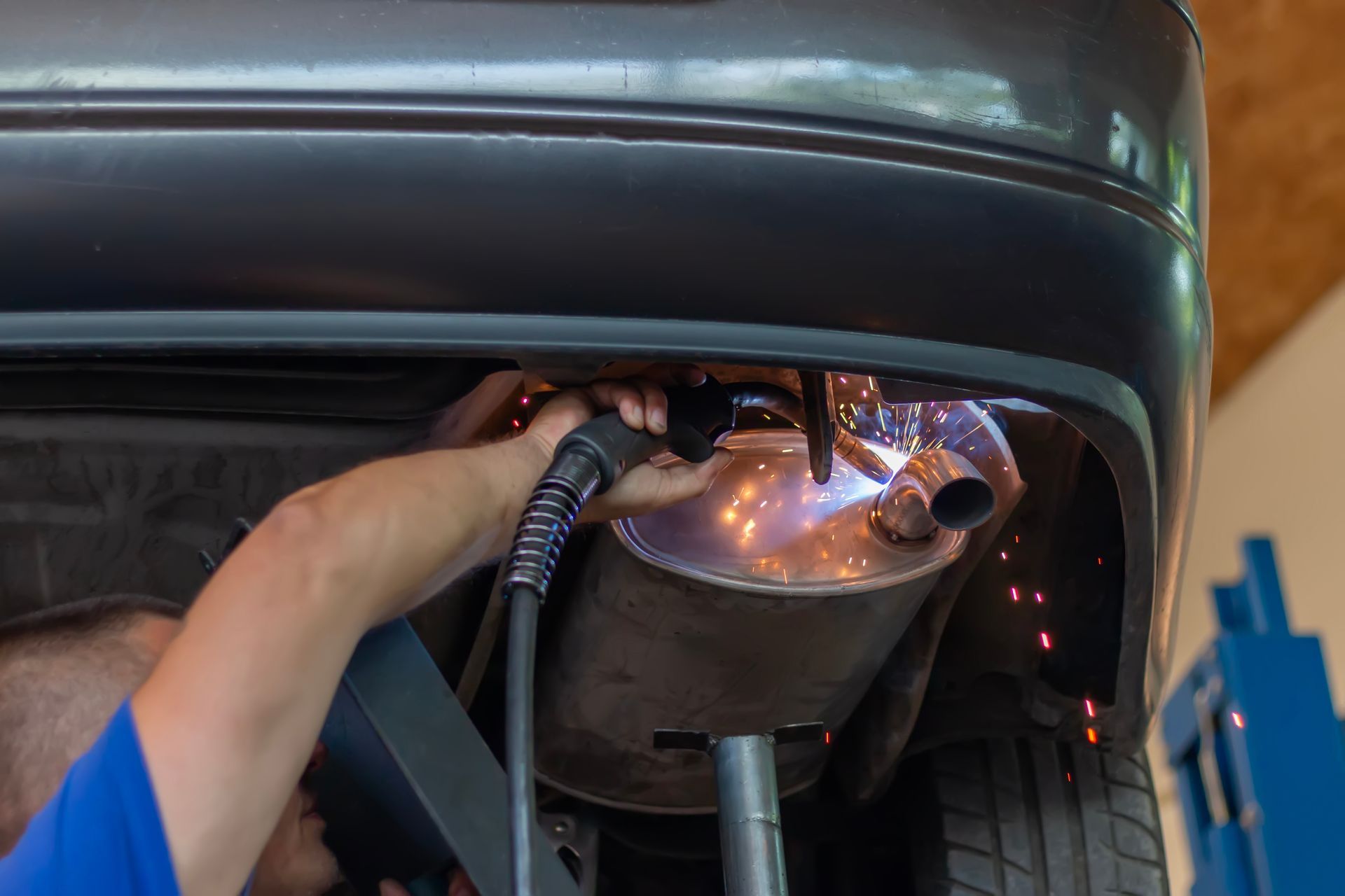 A mechanic at a muffler repair shop is replacing the rear muffler of the exhaust system in a car. A mechanic at a muffler repair shop is replacing the rear muffler of the exhaust system in a car.