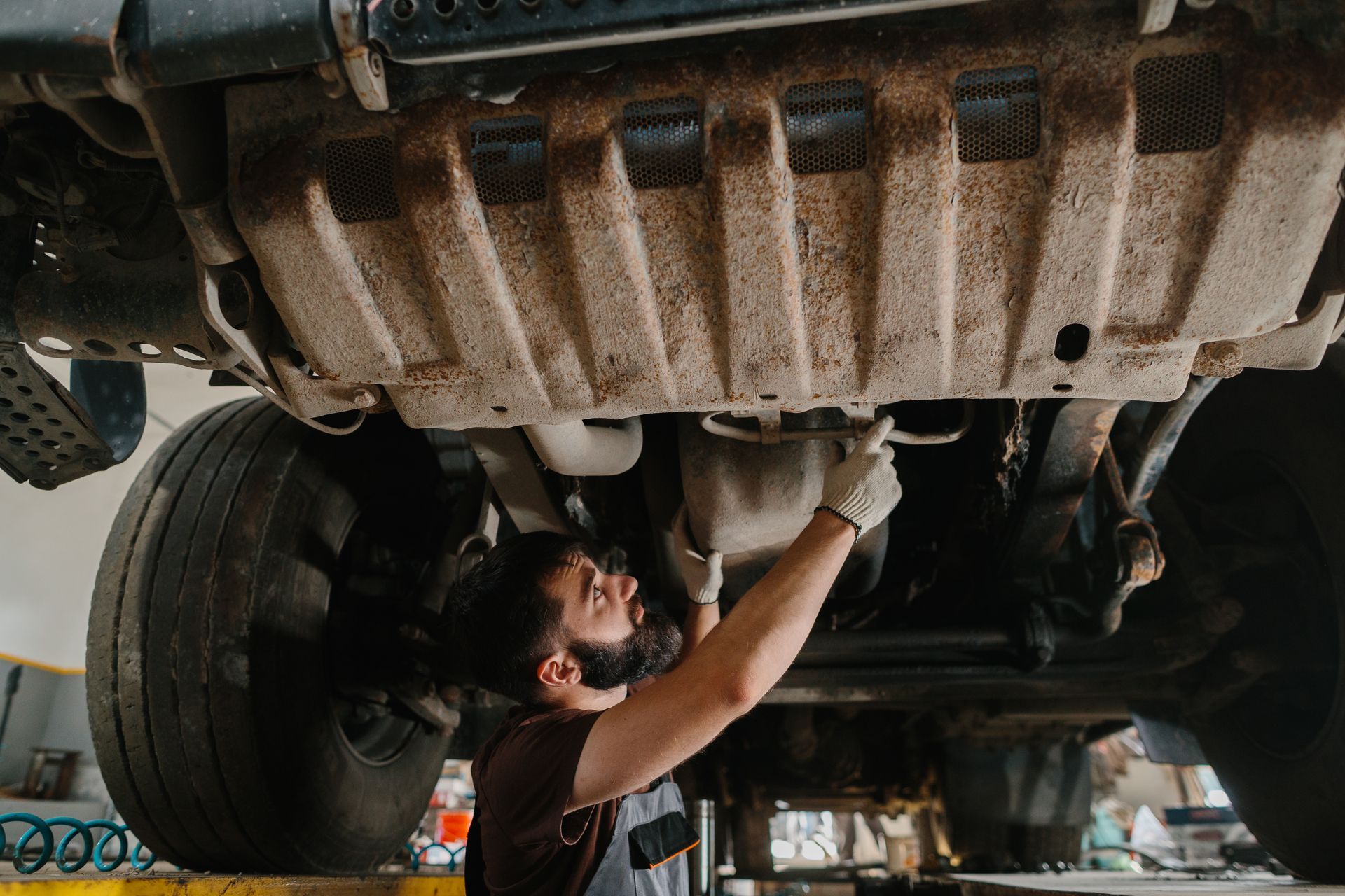 Technician inspecting vehicle exhaust system in auto repair shop. Technician inspecting vehicle exhaust system in auto repair shop.