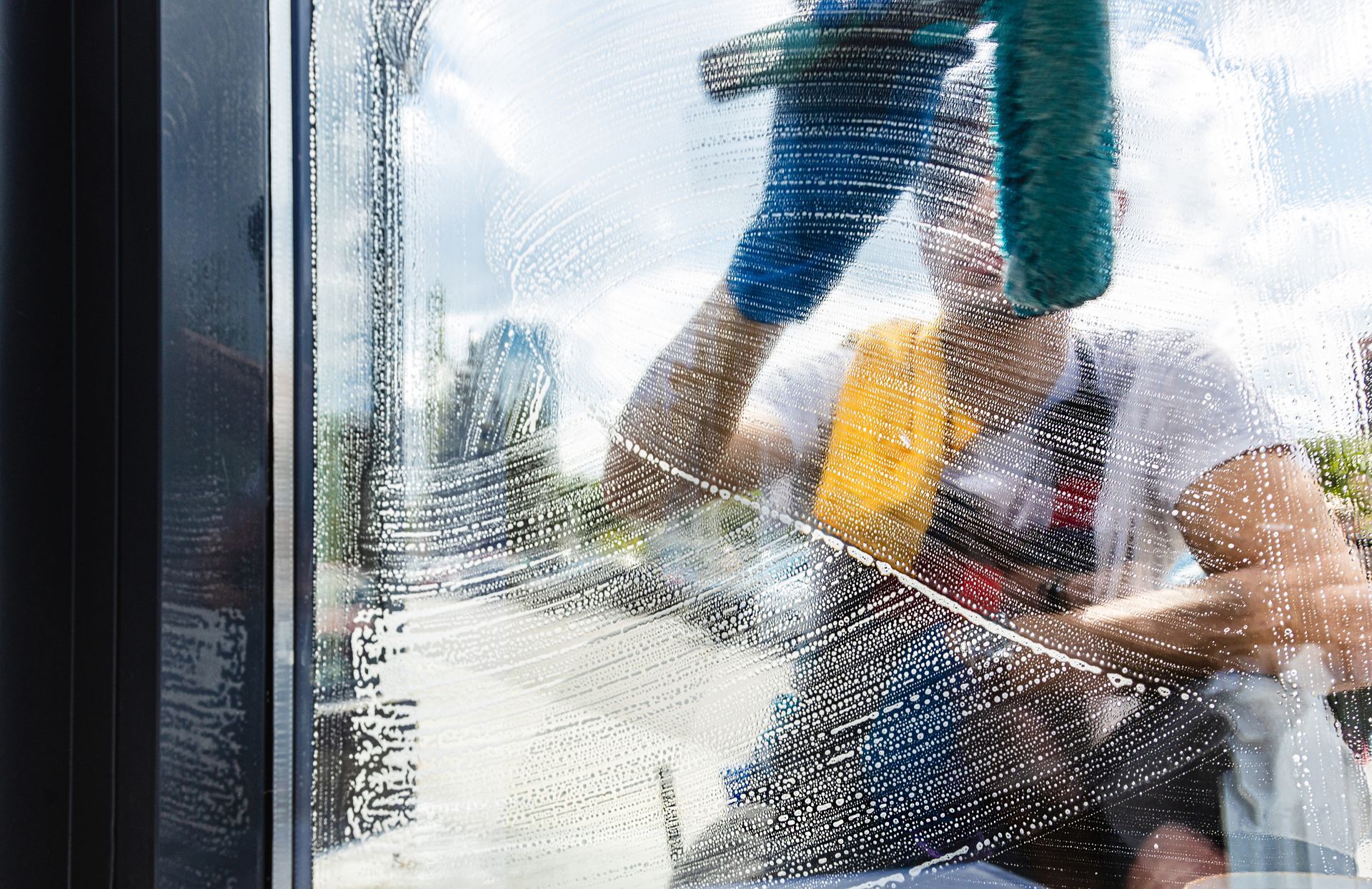 Residential cleaning service worker washing a soapy window with a squeegee