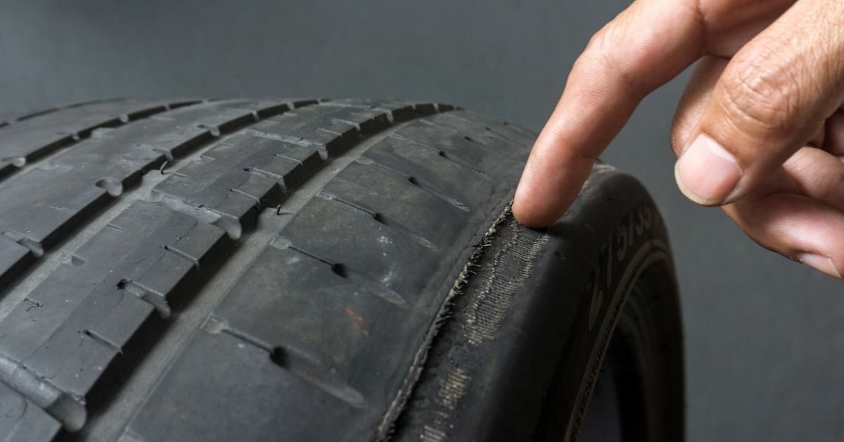 A hand pointing to a worn tire tread with exposed fibers along the outer edge.