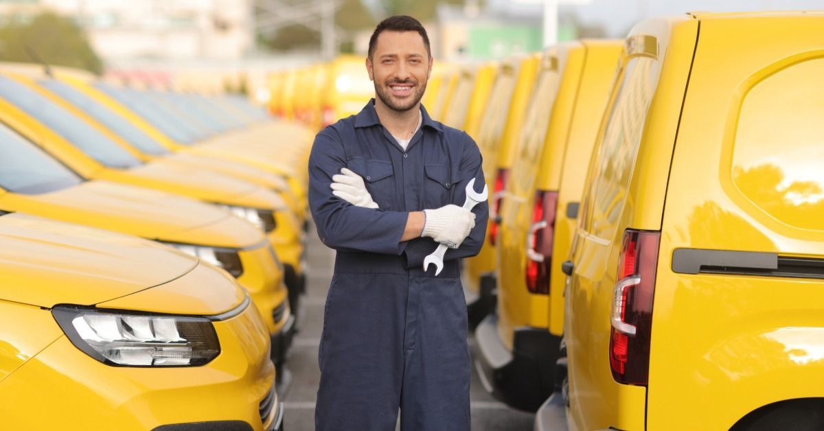 A person in blue coveralls stands between rows of yellow vans holding a wrench.