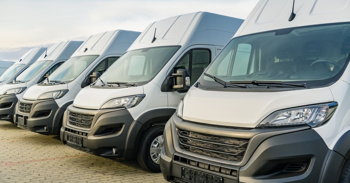 A row of commercial white vans are parked next to each other on a brick road.