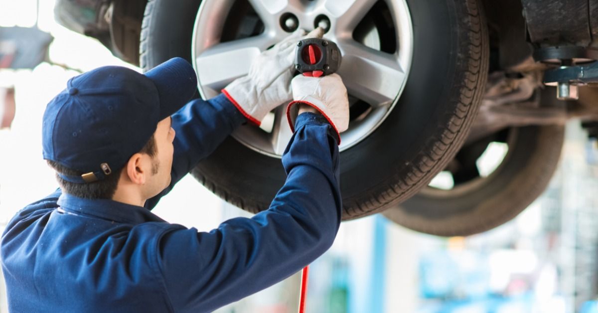 Mechanic changes a car wheel on a lift inside an auto repair shop bay.