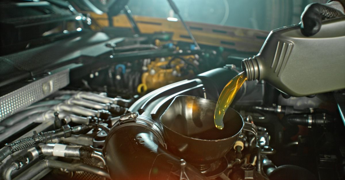 Mechanic pours engine oil into an open engine bay inside an automotive workshop.