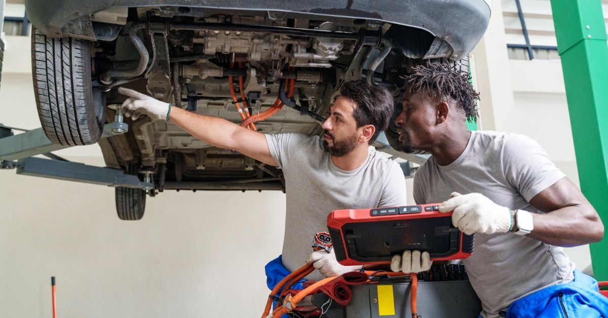Two technicians inspecting the underside of a raised vehicle in a workshop.