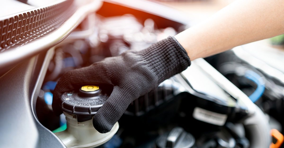 A technician with black gloves is checking the brake fluid reservoir of a car.