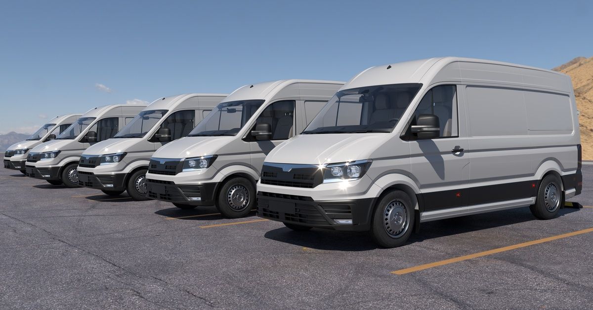 A row of white cargo vans parked in an outdoor lot under a blue sky.