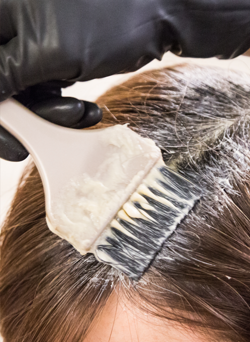 A woman is getting her hair dyed with a brush.